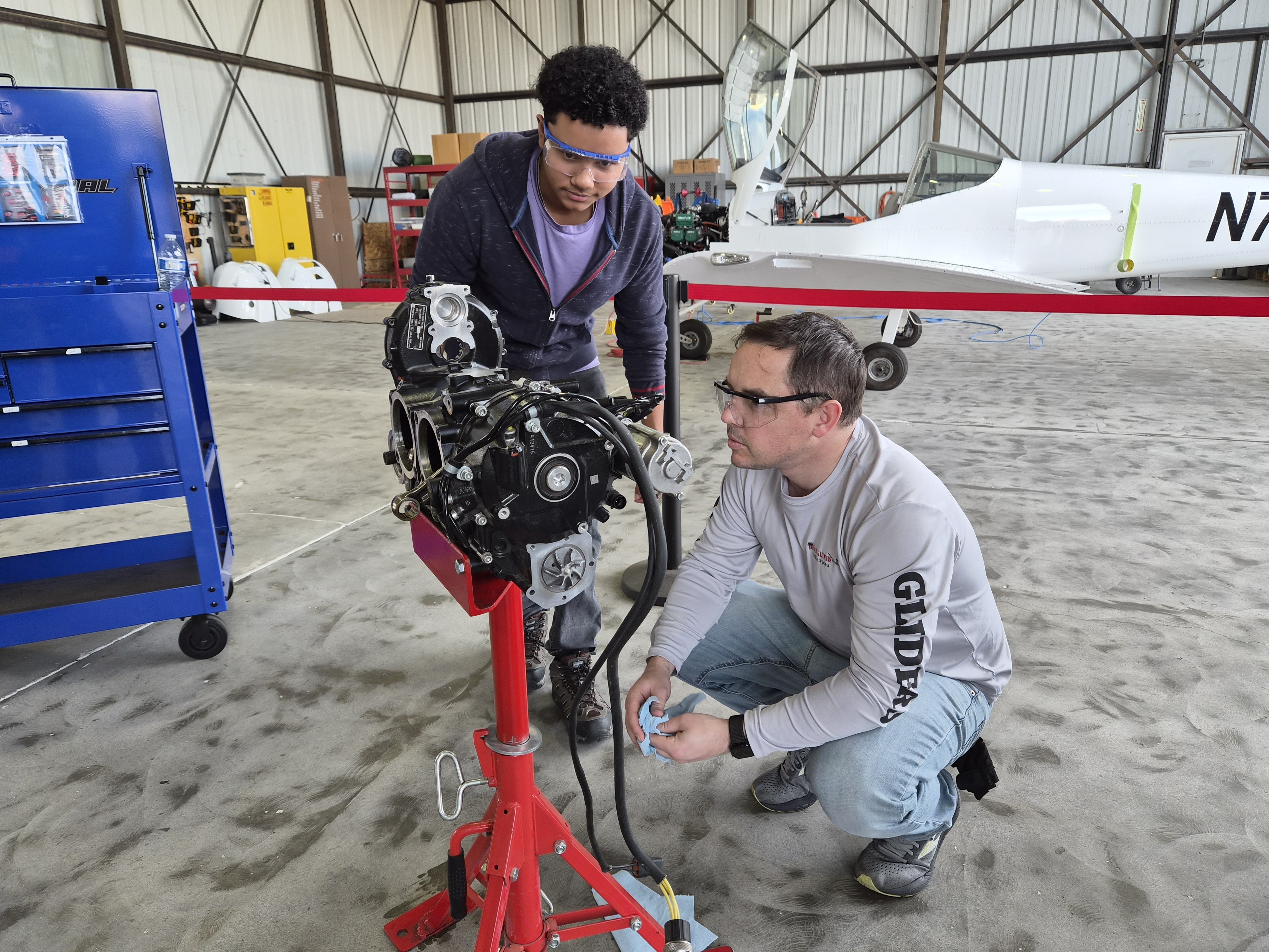 Instructor and student examining mounted aircraft engine in hangar